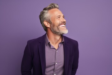 Handsome middle-aged man with gray hair and beard is laughing and looking aside while standing...