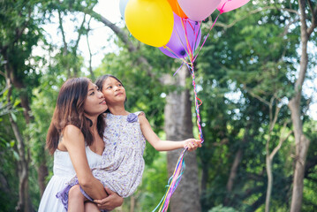 Happiness mother daughter play balloons together in green garden park outdoor lifestyle. Happy family two people enjoy have fun cheerful smile. Mother childhood hand holding colorful balloons outside