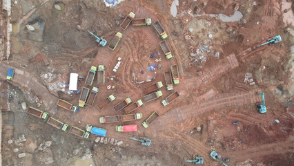 Aerial view Queue of trucks transporting excavated soil in a large construction area. There are excavators and lots of dirt trucks.