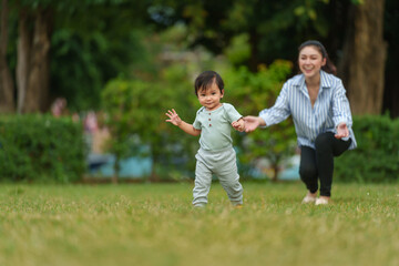 infant baby learn walking first step on grass field with mother helping in park