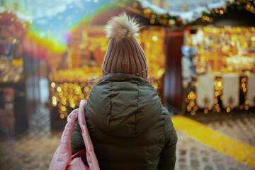 woman in green coat and brown hat at winter fair in city - obrazy, fototapety, plakaty