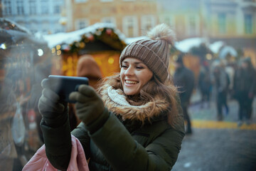 happy modern woman at christmas fair in city using video chat