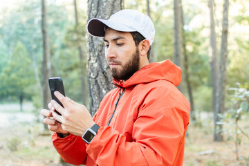 Joven con barba usando su teléfono celular en el bosque