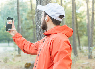 Hombre joven con barba tomando una selfie en el bosque.