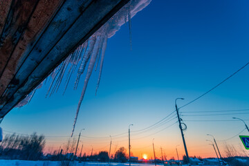 Melting icicles hanging down from roof with city background. Sunny day. Spring, warming concept....