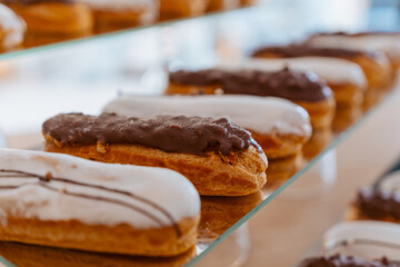 Eclairs with white and chocolate icing are laid out in a row on a mirror surface, display in a...