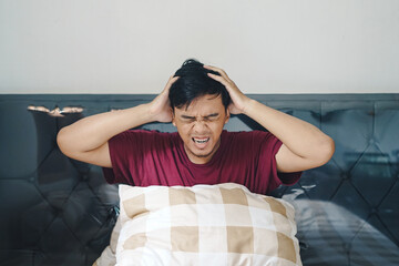 Portrait Asian Indonesian man on bed holding his head dizzy confuse depressed gesture - obrazy, fototapety, plakaty