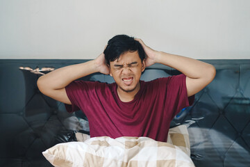 Portrait Asian Indonesian man on bed holding his head dizzy confuse depressed gesture