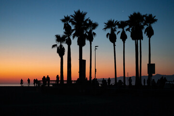 Silhouettes of people watching the skateboarders at the Venice beach skate park during sunset in California.