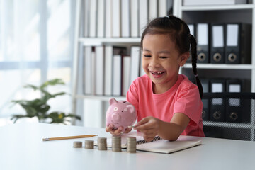 Cute little Asian girl playing with coins, making money in piles, putting money in a piggy bank....
