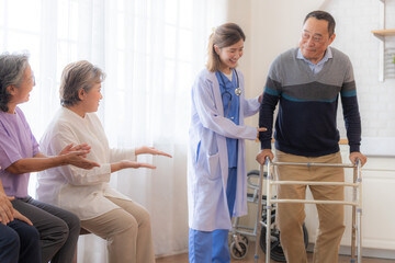 Asian young nurse support senior older man walk with walker. Beautiful nurse help and take care. elderly mature grandpa patient doing physical therapy with a group of senior friends in hospital.