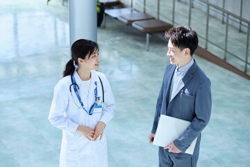 病院内にてスーツを着たMRの男性と話をする女性医師