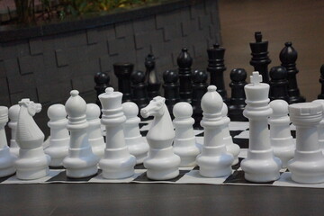Large chess set with large white chess pieces in foreground, large black chess pieces in background