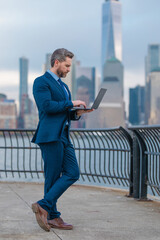 Businessman in suit holding laptop on urban street in NYC. Successful business man outdoor. Middle...