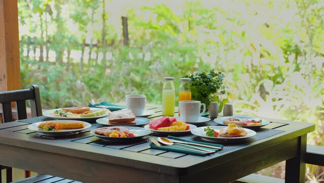 Outdoor brunch table set for four people with healthy selection of salad, scrambled eggs, pastries, and fresh juice amidst garden. Al fresco dining and healthy eating.