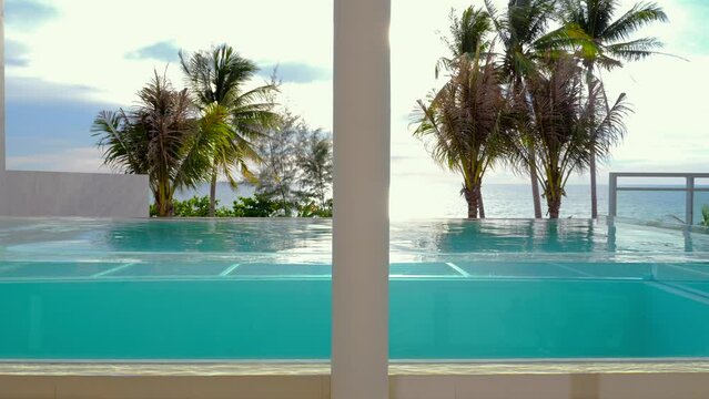 Tropical resort view with infinity pool overlooking ocean, framed by palm trees and calm skies. Luxury travel and relaxation.