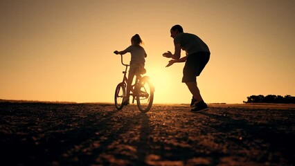 Happy family green park at sunset.Dad teaches daughter to rid bike in summer park.kid rides bicycle on green grass.Green energy.Dad teaches his daughter to ride bike for first time in park at sunset.