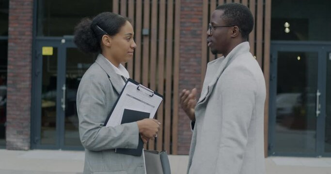 Man and woman businesspeople walking shaking hands talking holding documents in street outside office center. Business partnership and communication concept.
