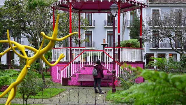 Female tourist poses in front of pink kiosk in Jardim Duque da Terceira