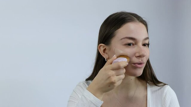 European Caucasian young woman applying makeup foundation with sponge isolated on grey background