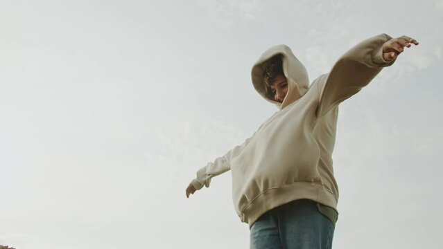 A stylish teenager boy in the background stands with his hands up during a strong wind and his clothes flutter