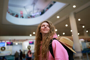 Smiling tourist with backpack gazes upward in bustling airport decorated for festive season, ready...