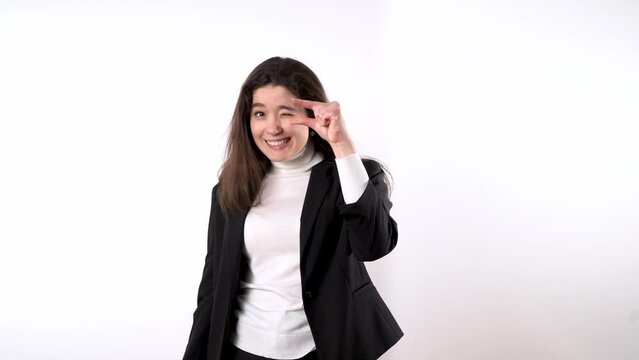 Smartly dressed smiling young brunette against white background using her forefinger and big finger to show that something is tiny and laughing afterwards