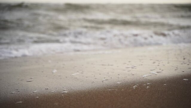 Gentle waves wash over sandy shore, frothy sea foam bubbles on beach. Calm seaside ambiance, tranquil nature scene. Serene coastal landscape, soothing ocean, tide ebbs and flows, water textures.
