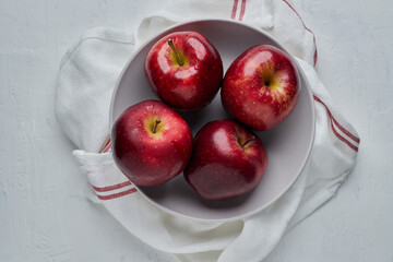 Red apples in a white bowl placed on a red white cloth on a white background.