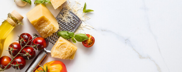 Cooking background with parmesan cheese, basil leaves, cherry tomato, garlic, olive oil and iron grater on marble table top view