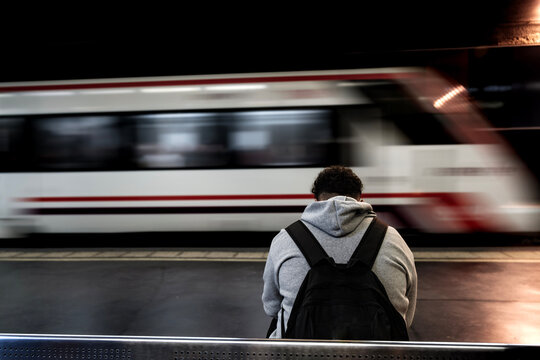 Estaci&oacute;n de tren Victoria Kent, M&aacute;laga, hombre sentado viendo pasar el tren, visto de espaldas, mochila negra