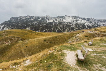 A lone bench atop a grassy hill, surrounded by snow-capped mountains and a vast tundra landscape, invites one to pause and admire the breathtaking