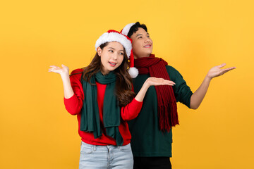 Excited happy young Asian couple wearing Christmas theme clothes  isolated on yellow background