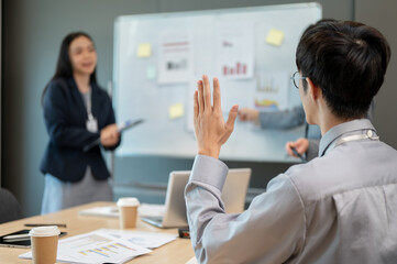 A young businessman raising his hand to ask a question during the presentation in the meeting