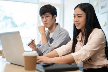 Two happy young Asian male and female colleagues are working on a project together.