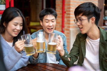 Group of happy young Asian friends are enjoying drinking beers and talking at a bar together.