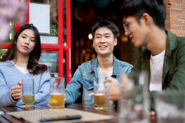 Group of happy young Asian friends are enjoying talking and drinking beers at a bar together.
