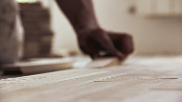 Carpenter worker installing wood parquet board during flooring