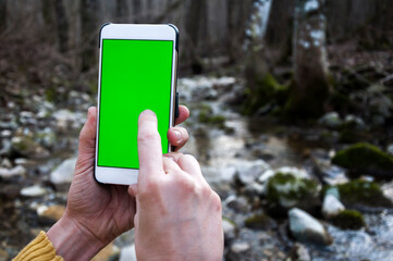 Adult Woman Hands Using a Smart Phone in Nature with Green Screen Over a Water stream