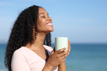 Happy black woman smelling coffee on the beach