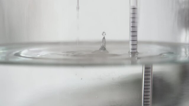 alcohol distilling process closeup - liquid distilled transparent liquid flowing in large glass jar with floating alcoholometer in it.