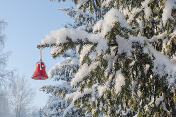 A red Christmas tree toy bell hangs on a snow-covered spruce branch in the forest after a heavy snowfall. Snow covering a pine tree in the forest. Beautiful winter landscape. Snow fairy tale.