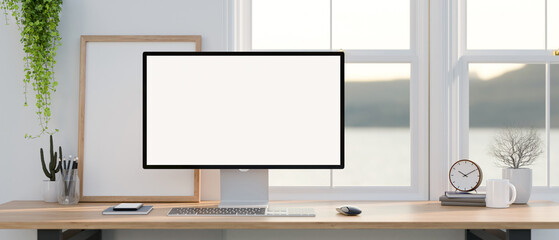 A PC computer mockup with accessories on a wooden desk against the window in a modern white room.