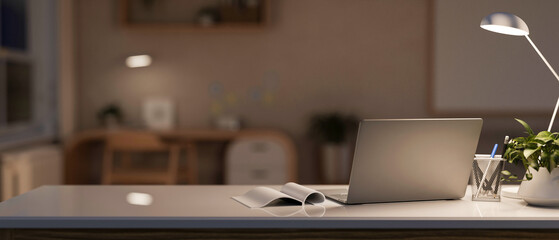 Back view of a modern, cosy home workspace at night with a laptop computer and accessories on a desk