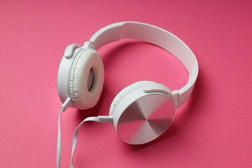 White, on-ear headphones with a wire on a pink background.