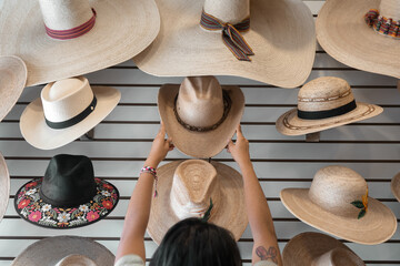 A young Hispanic woman is choosing a hat in a shop