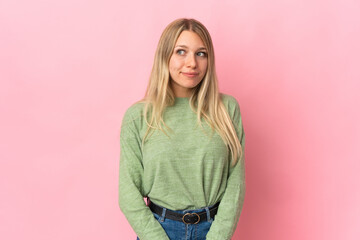 Young blonde woman isolated on pink background making doubts gesture looking side