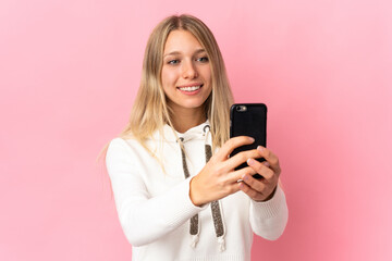 Fototapeta premium Young blonde woman isolated on pink background making a selfie with mobile phone