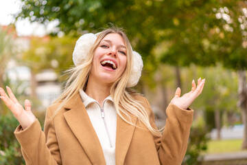 Young pretty blonde woman wearing winter muffs at outdoors smiling a lot
