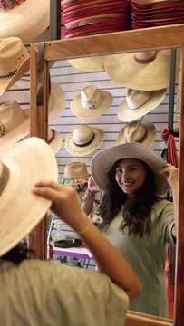 A young Hispanic woman is looking in the mirror trying on a new hat